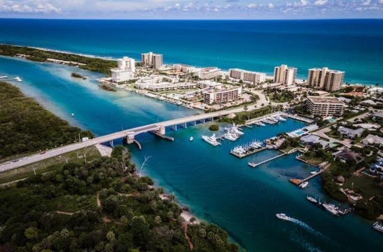 An aerial view of a South Florida coastline, with residential buildings, boats, and a nearby forest. Photo via Unsplash.